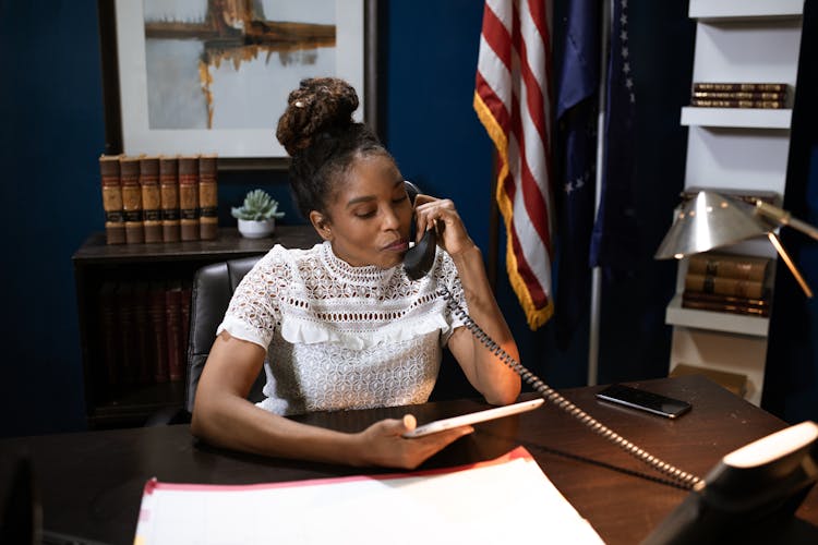 A Woman In White Shirt Sitting On A Chair While Talking On The Phone