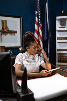 Black female executive at desk talking on phone, tablet in hand.