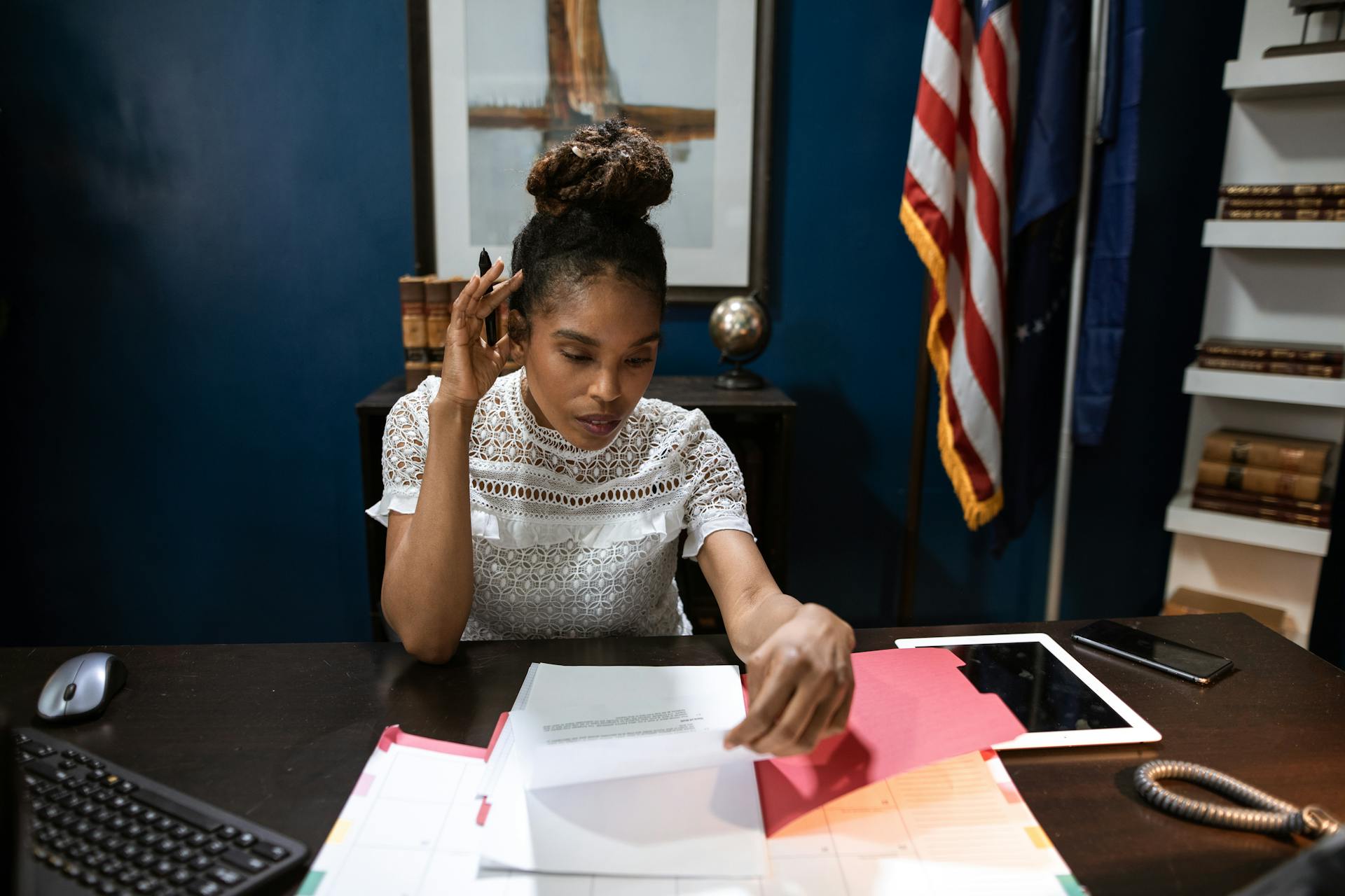 Businesswoman examines reports at desk with American flag in background.