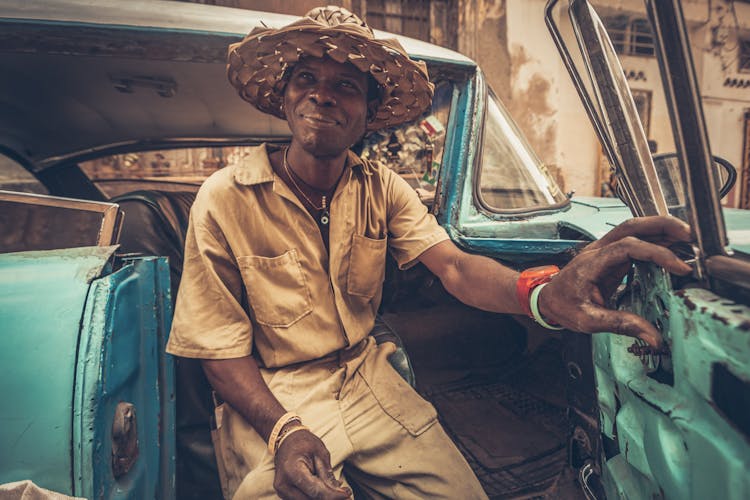 Man In Woven Sunhat Sitting On An Old Car 