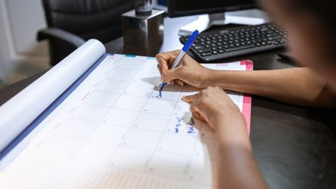 Close-up of a woman planning her schedule on a desk calendar in an office setting.