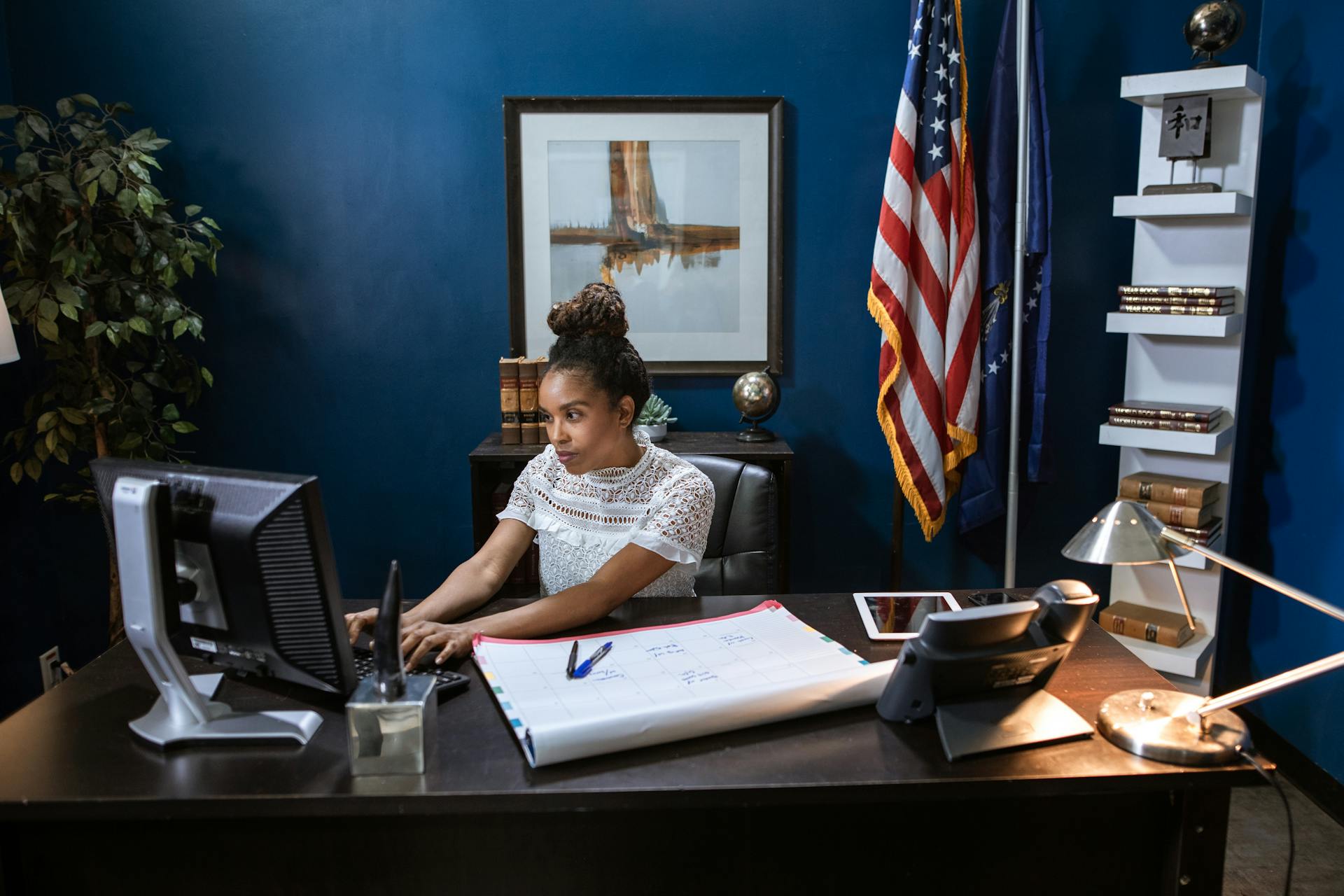 An African American woman concentrating on her work at a desk with computer and documents.