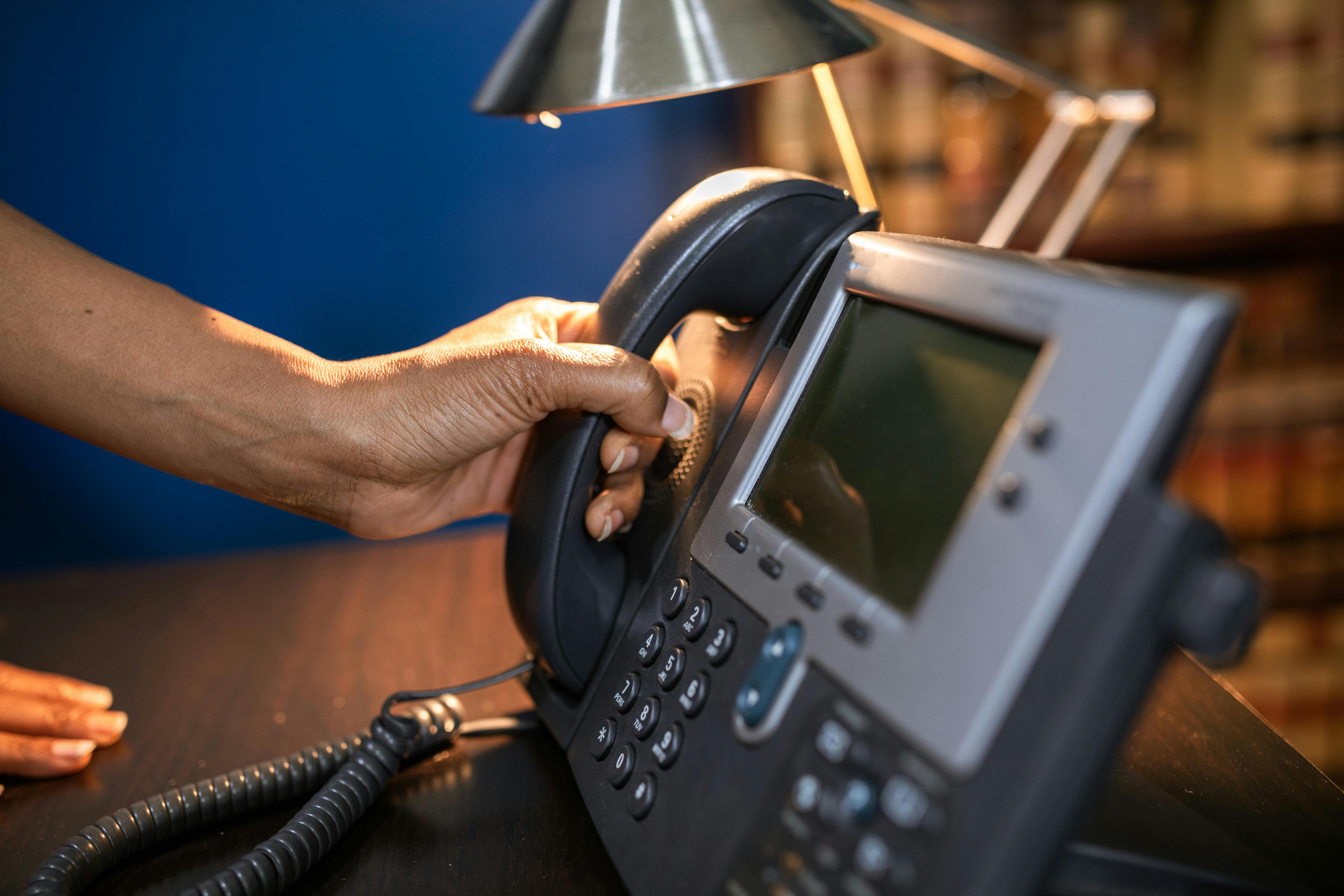 A close-up image of a hand picking up a handset from an office telephone, emphasizing communication device usage.