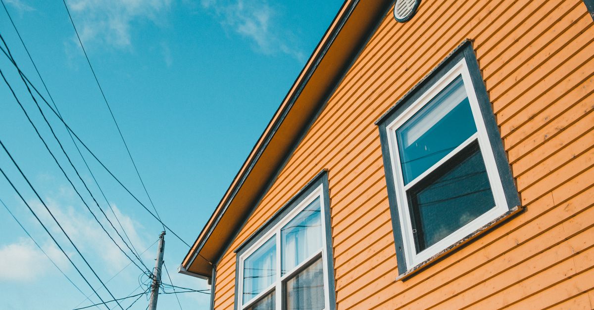 Low-angle shot of a yellow wooden house exterior with power lines against a blue sky.