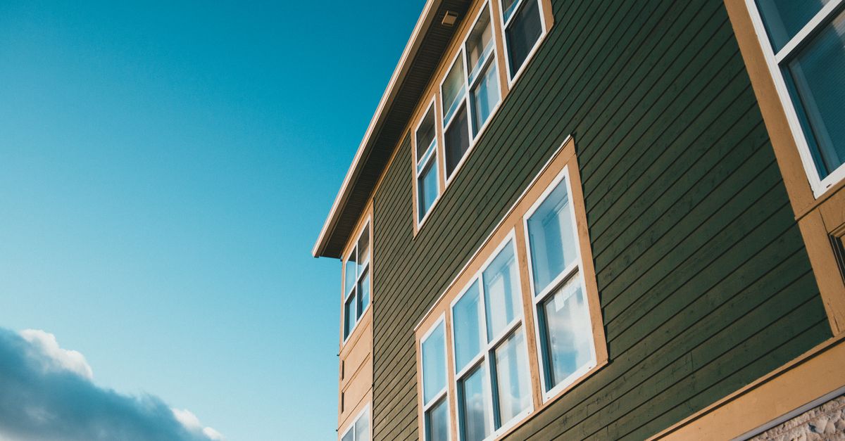 Low angle view of a green wooden house with multiple windows under a vibrant blue sky.