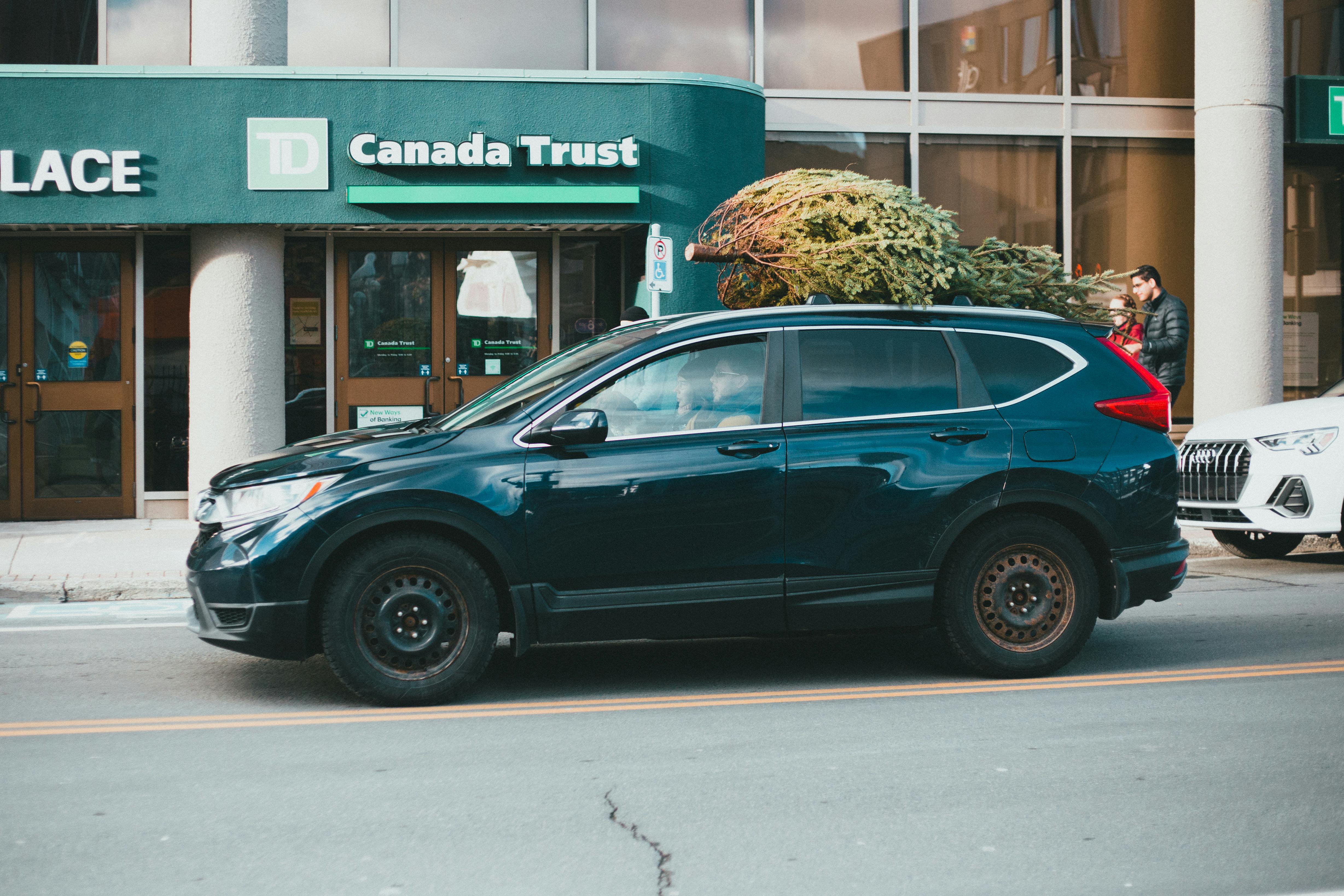 A car with a Christmas tree on its roof, parked in front of a bank, representing bank financing during the holiday season.