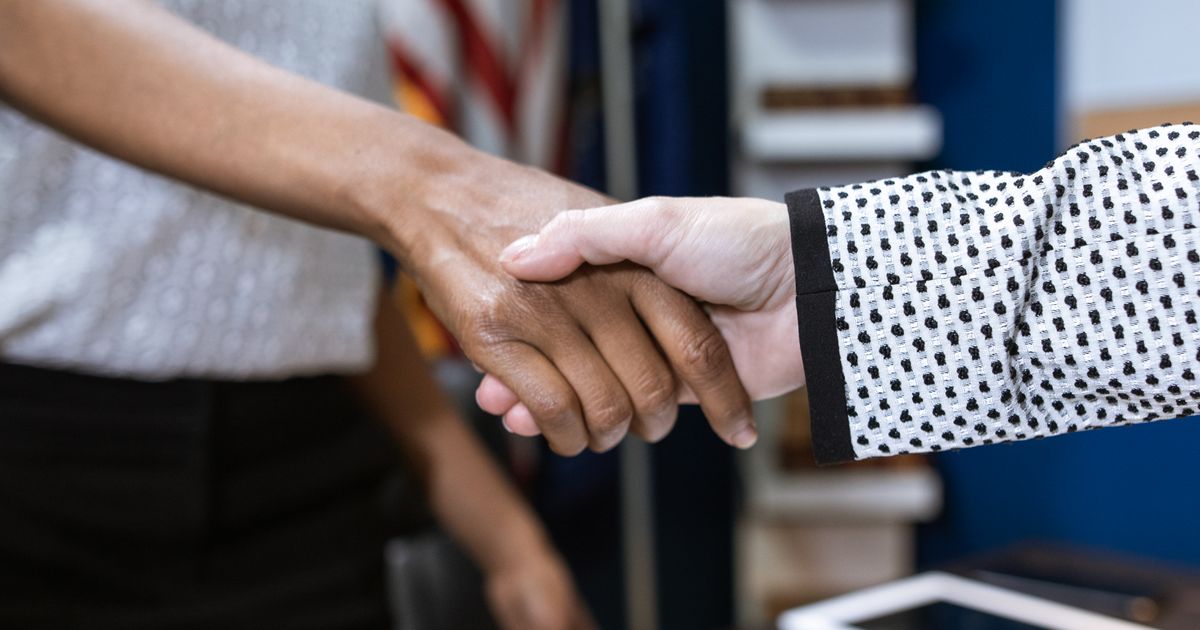 Two people shaking hands across an office desk
