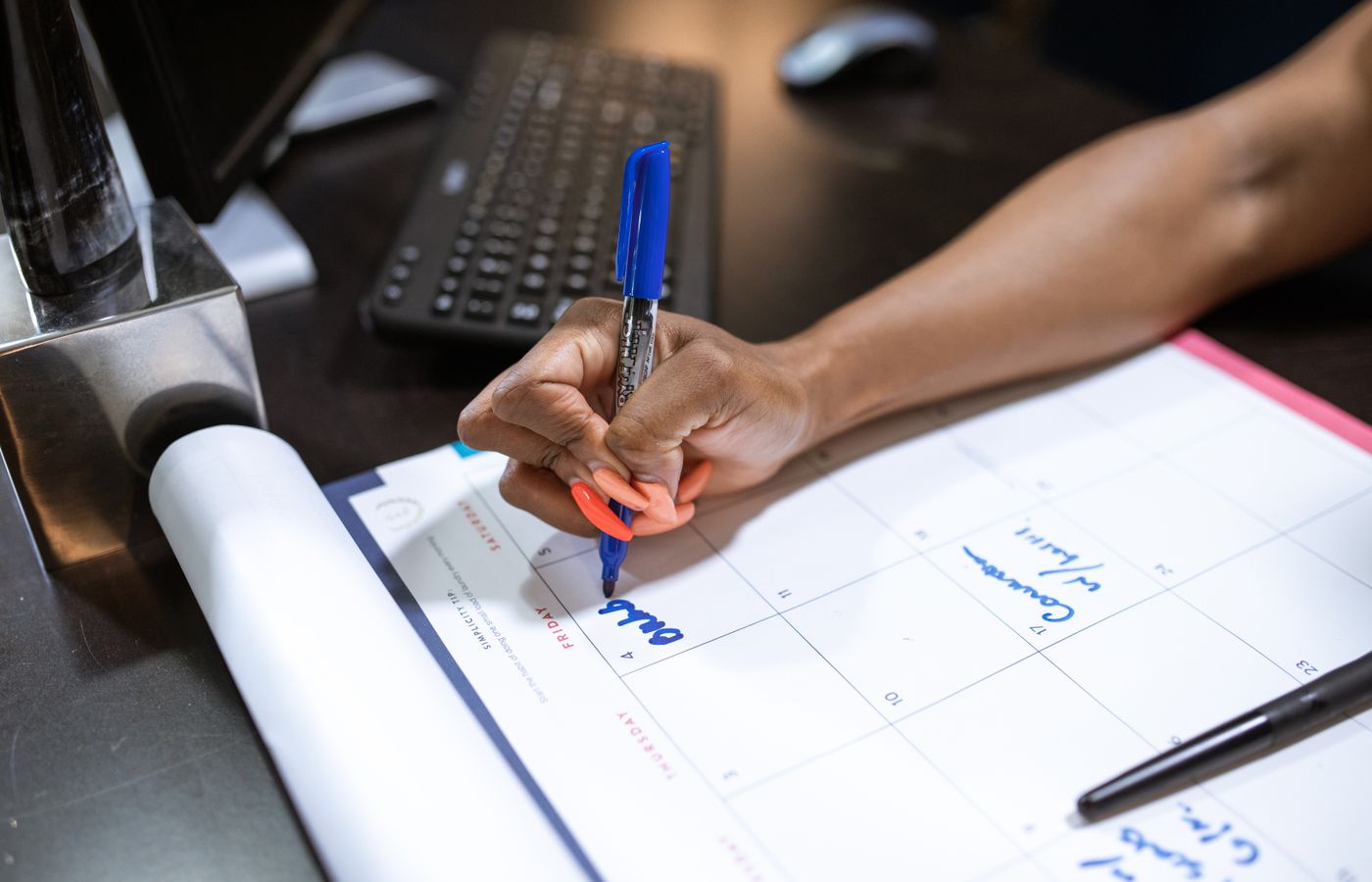 Detailed shot of a person's hand writing notes on a calendar using a blue marker.