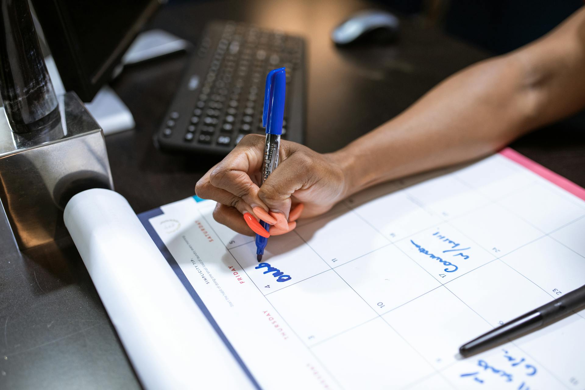 Detailed shot of a person's hand writing notes on a calendar using a blue marker.