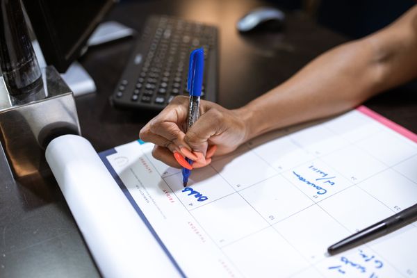 Mână care notează date într-un calendar de planificare cu marker