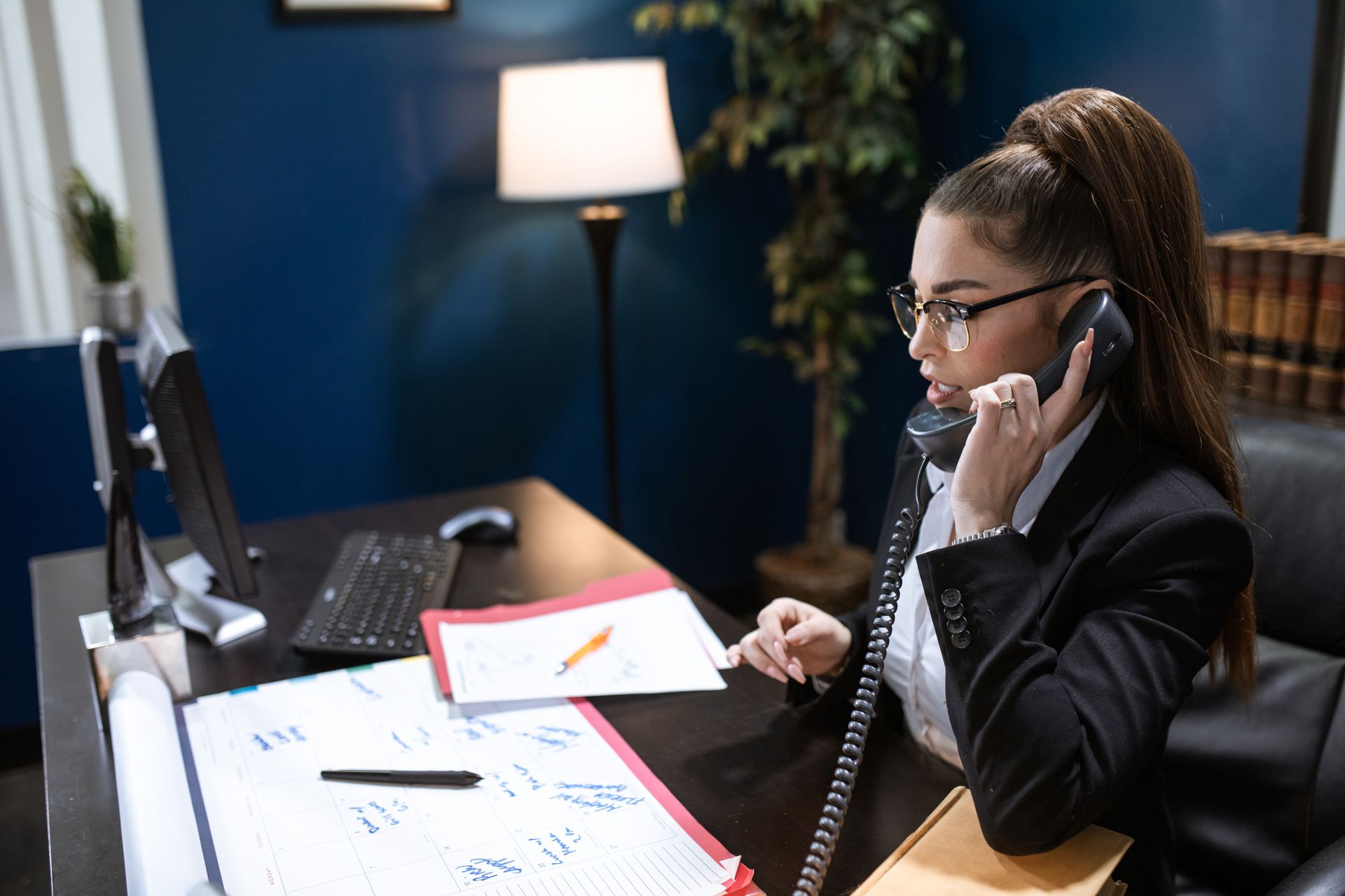 Businesswoman in a black blazer discussing work on a telephone in a modern office setting.
