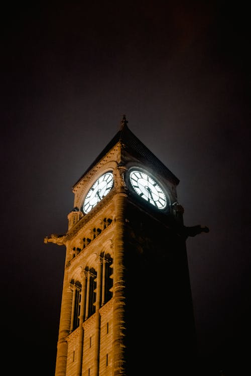From below of tall illuminated medieval clock tower located against cloudless dark sky on street at night time in Toronto
