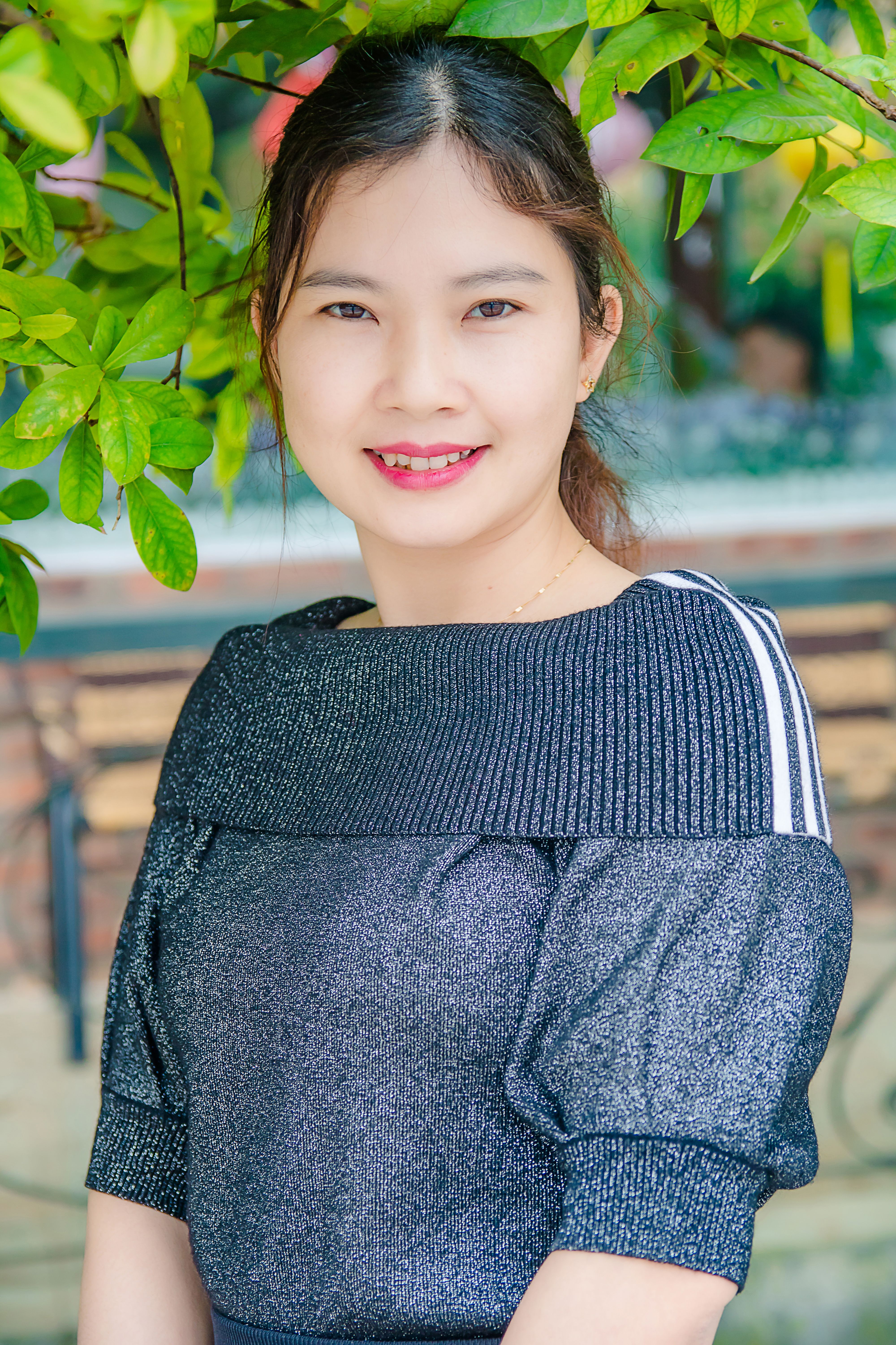 Portrait of a smiling woman in a blue top surrounded by green leaves, conveying natural beauty.