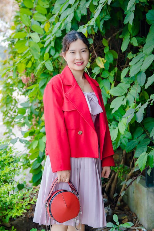 A Woman in Red Blazer Standing Near Green Leaf Plant