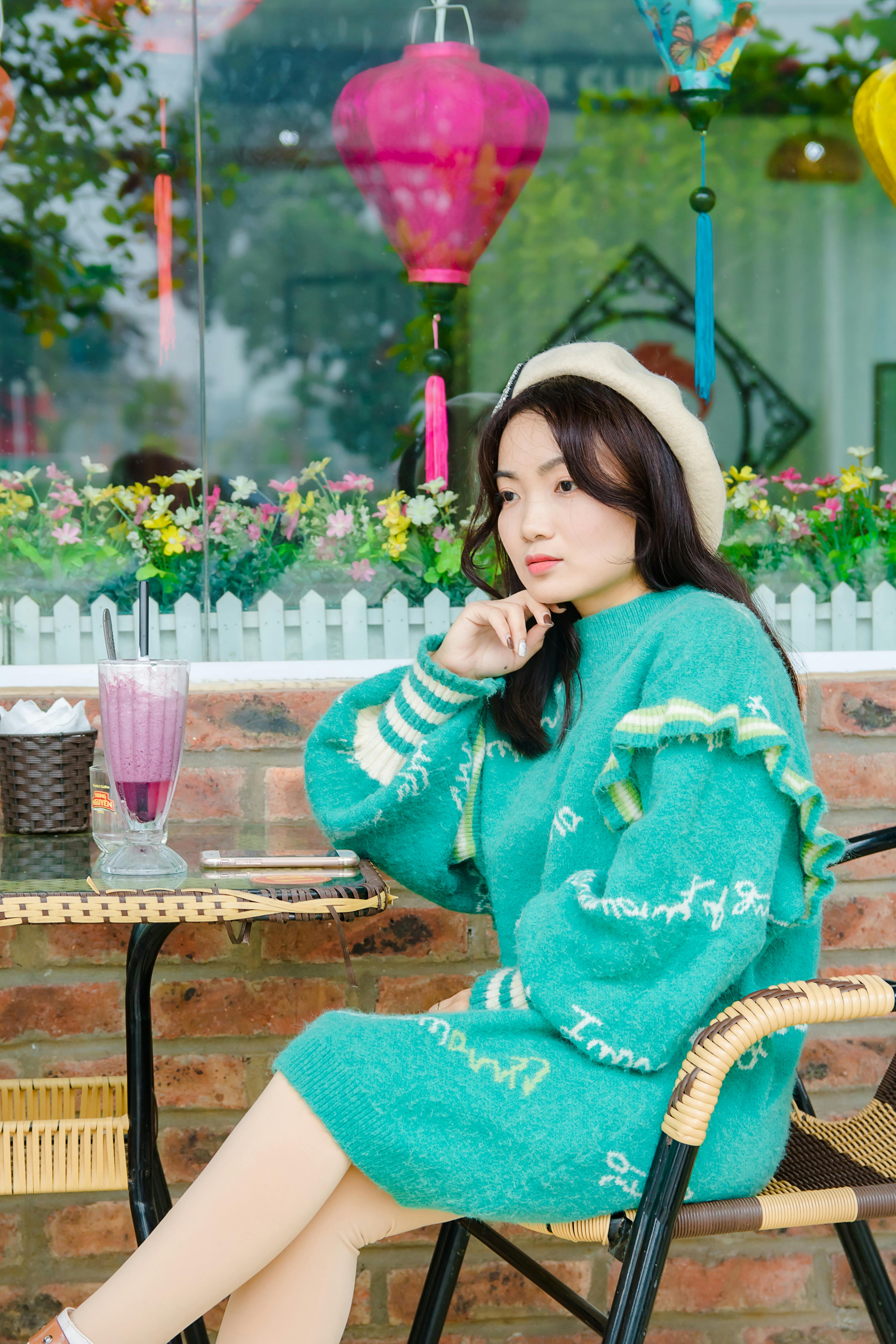 A fashionable woman in a cozy green knitted sweater enjoys a day at a colorful outdoor café.