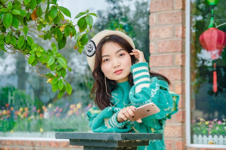 Pretty Woman In Green Sweater Holding A Mobile Phone While Looking At Camera