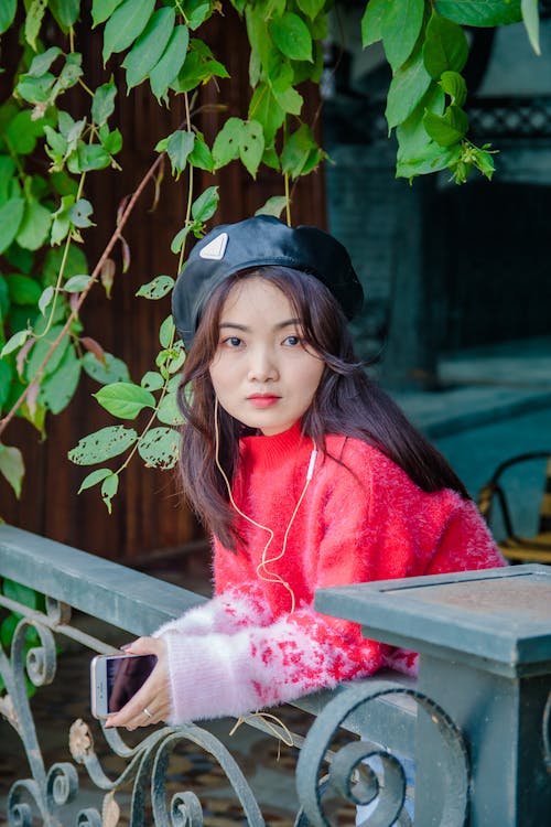 Pretty Woman in Red Sweater Holding a Mobile Phone while Looking at Camera