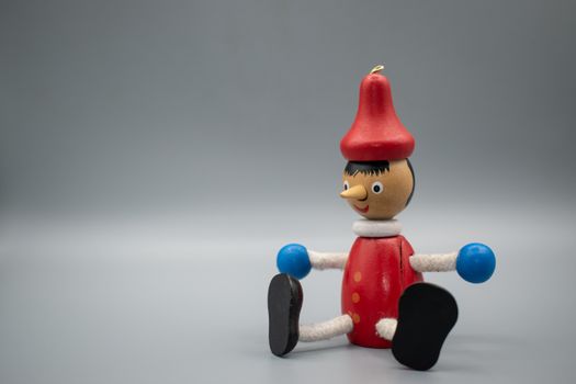 Close-up of a colorful wooden Pinocchio toy with movable arms and legs on a plain backdrop.