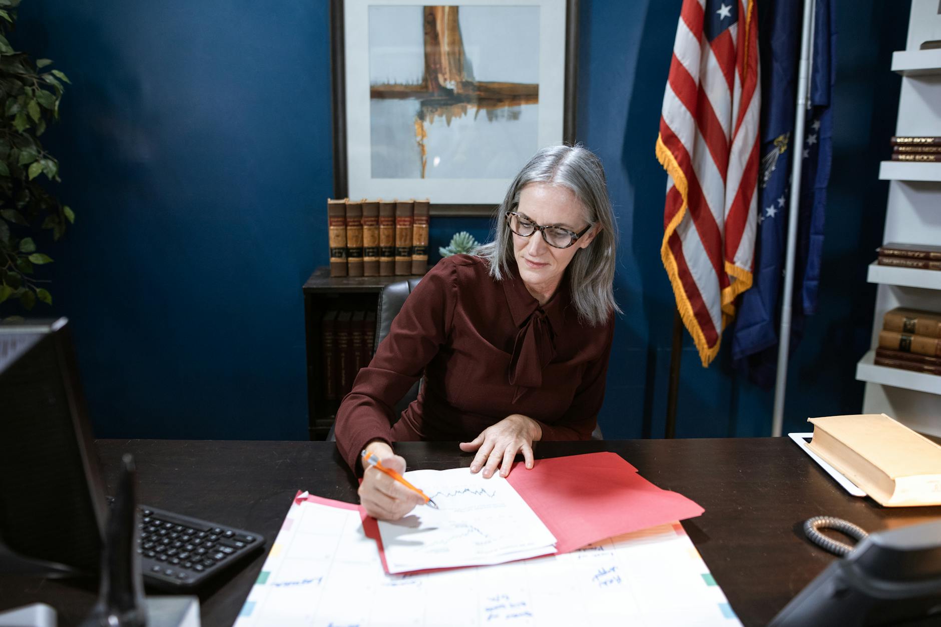Senior woman in an office setting reviewing documents with US flag background.