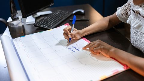 Person writing important notes in a desk calendar with a pen, set in an office.