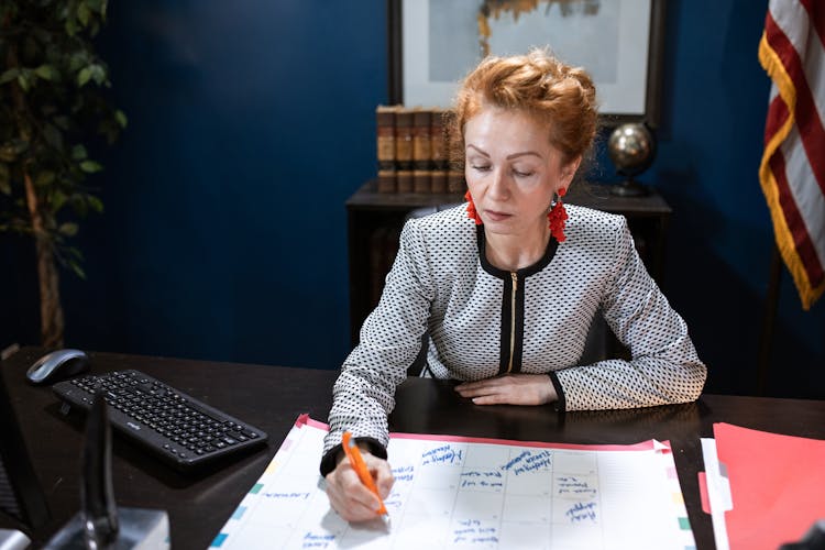 A Woman In Long Sleeve Shirt Writing On Calendar