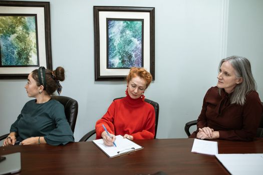 Three women in an office meeting, discussing and taking notes.