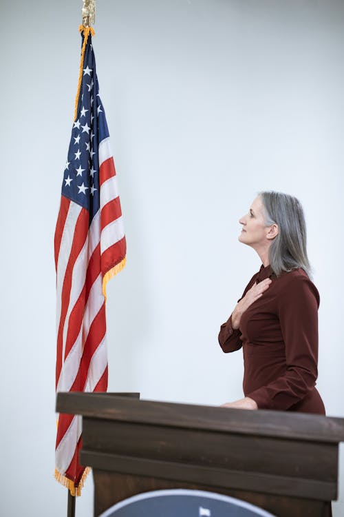 Woman in Maroon Long Sleeve Shirt Standing Near a Flag