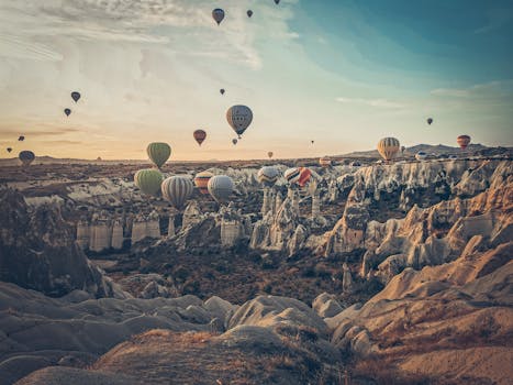 Breathtaking view of hot air balloons floating over Cappadocia's unique rock formations at sunrise.