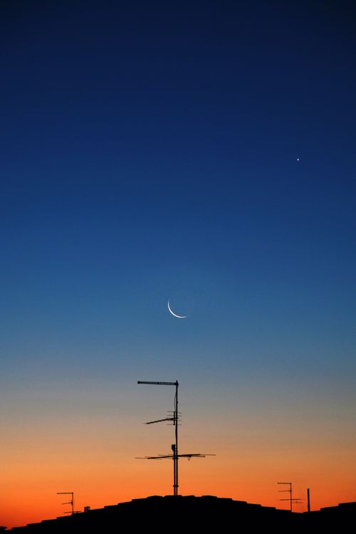 Free Silhouette of rooftop antennas under a crescent moon during twilight in Rizza, Veneto, Italy. Stock Photo