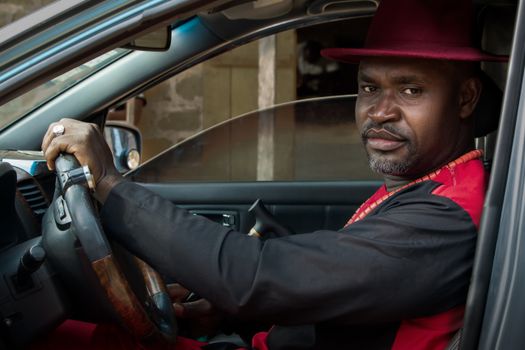African man in traditional attire driving a car in Douala, Cameroon.