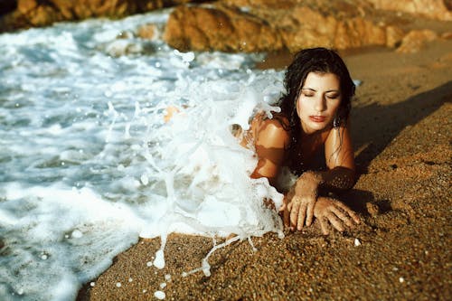 Sensual woman lying on beach in wavy ocean in sunny day