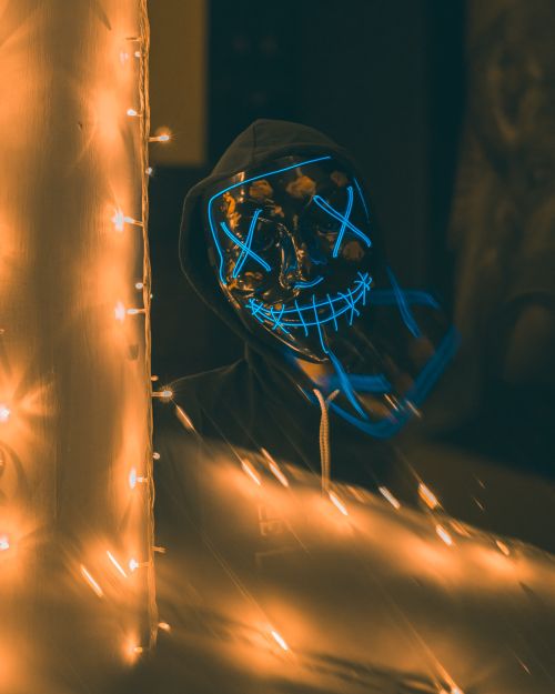 Free A dark and eerie scene of a masked figure surrounded by glowing lights, evoking mystery. Stock Photo