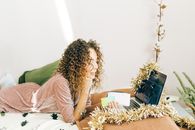 A woman with curly hair shops online using a laptop decorated with Christmas tinsel.