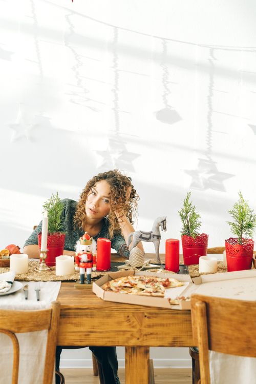 Free Woman with curly hair sits at decorated table with pizza and holiday candles. Stock Photo
