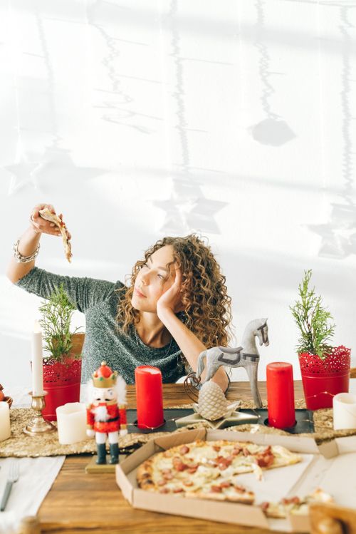 Free Woman with curly hair enjoying pizza in a festive setting with candles and decorations. Stock Photo