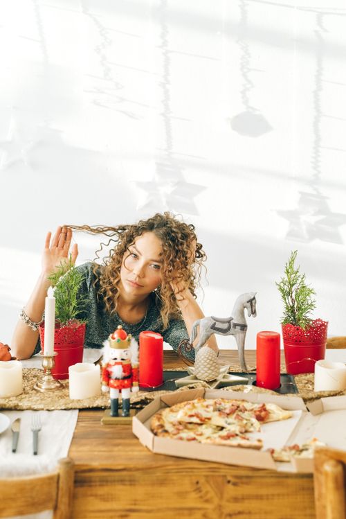 Free A pensive woman with curly hair sits at a holiday-decorated table with pizza and Christmas decorations. Stock Photo