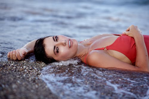 Woman lying on beach in water of sea and looking at camera