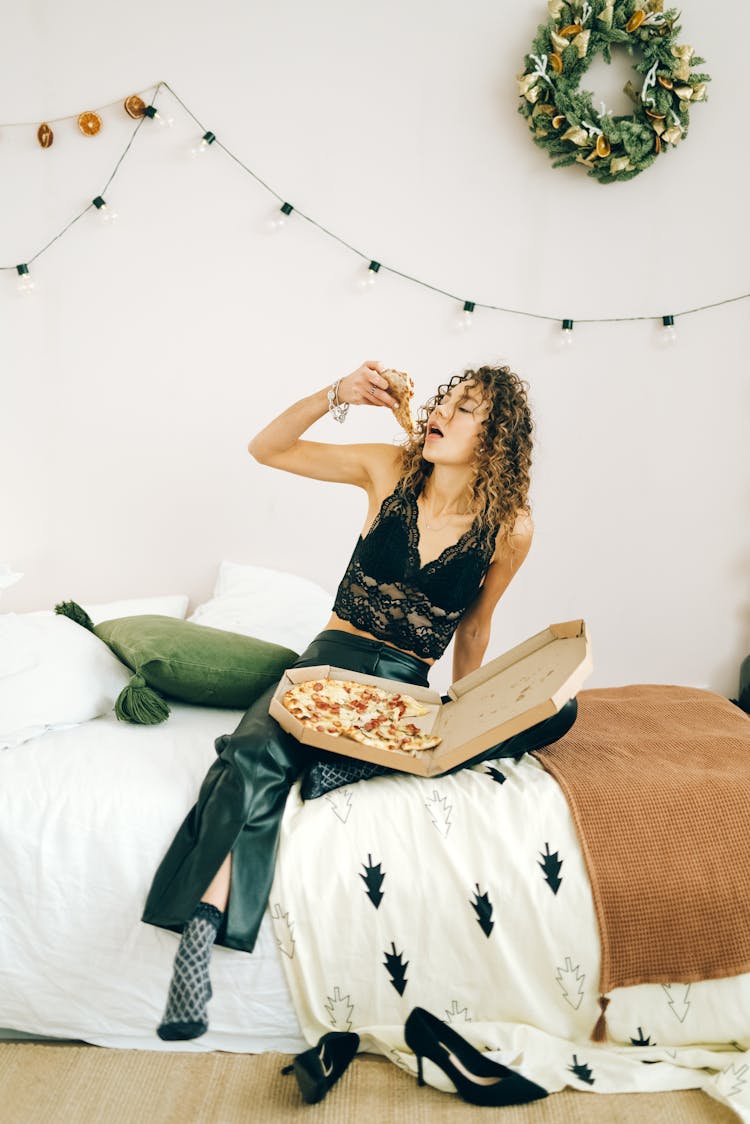 Woman In Black Lace Crop Top Sitting On Bed Eating Pizza