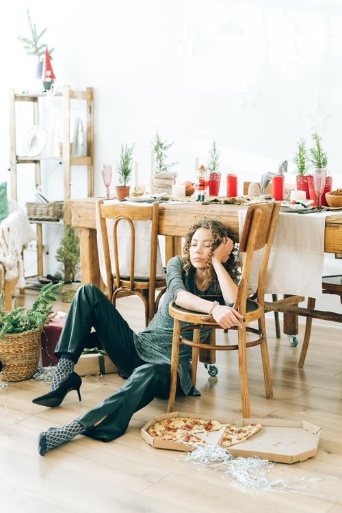 Free A woman with curly hair sitting on a wooden floor near a holiday-decorated table with pizza. Stock Photo