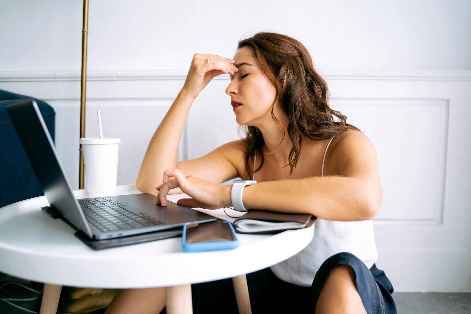 Woman experiencing work fatigue with laptop at a table, indicating stress and tiredness.