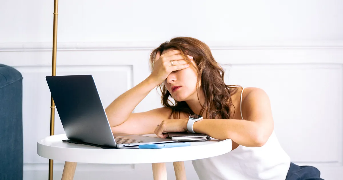Someone sitting at a laptop with their head in their hand, worn out