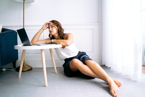 Woman in White Top with Hand on Head Sitting on the Floor 