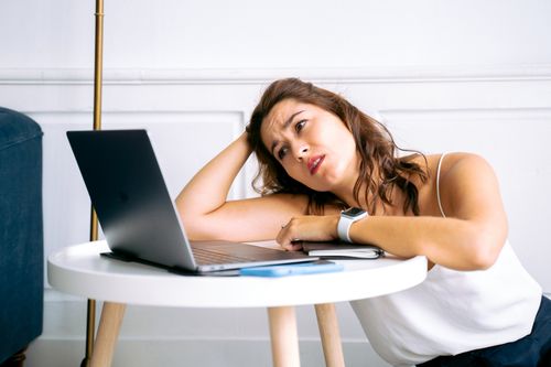 Free A frustrated woman sits at a desk with her hand on her head, staring at an open laptop. Stock Photo