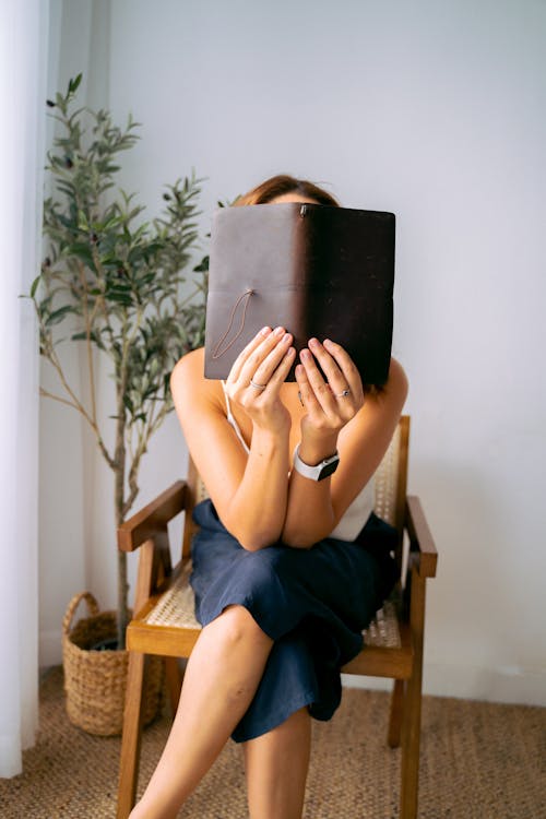 Free Person Sitting on a Wooden Chair Holding a Notebook Stock Photo