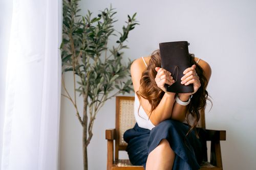 Free A woman sits in an armchair, head down, clutching a notebook, conveying emotion. Stock Photo