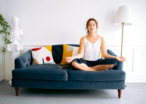 Free Woman in White Top on Lotus Pose on a Blue Sofa Stock Photo