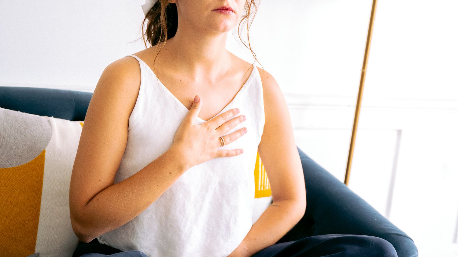 A woman seated on a couch with her eyes closed and her hands on her body