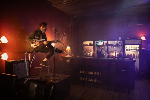 Man Playing Guitar on Stage While Sitting on Stool