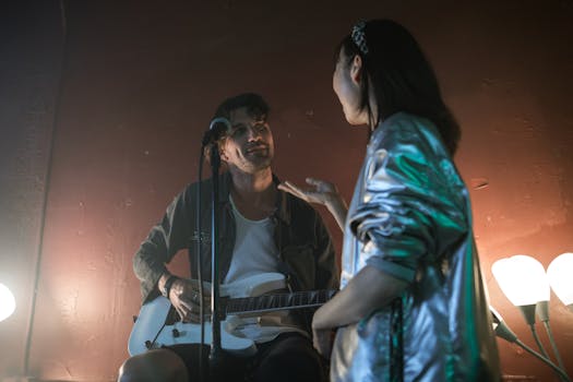 Musician playing guitar while interacting with a singer on a dimly lit stage.