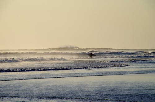 A Silhouette of a Surfer in a Shore with Crashing Waves
